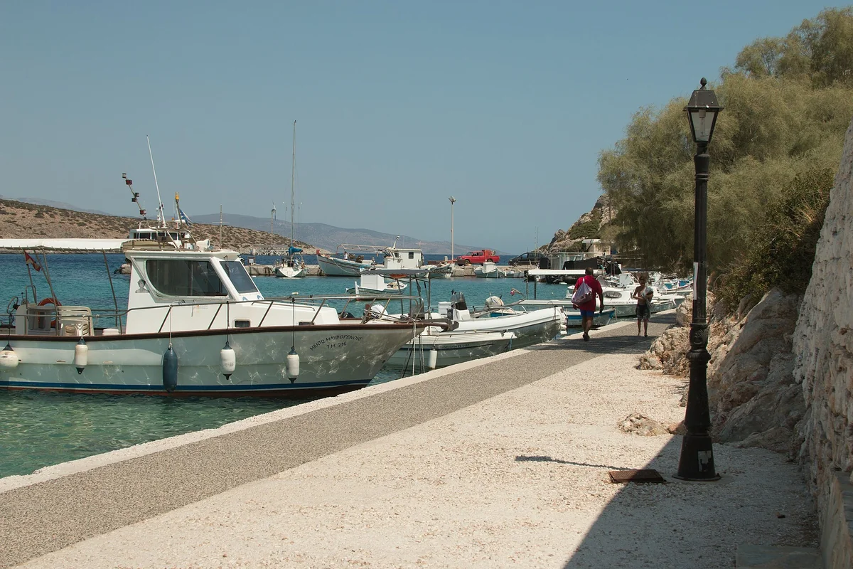 Fishing boats lie beside the waterfront path at Agios Georgios harbour on Iraklia, Greece; no cats are visible.