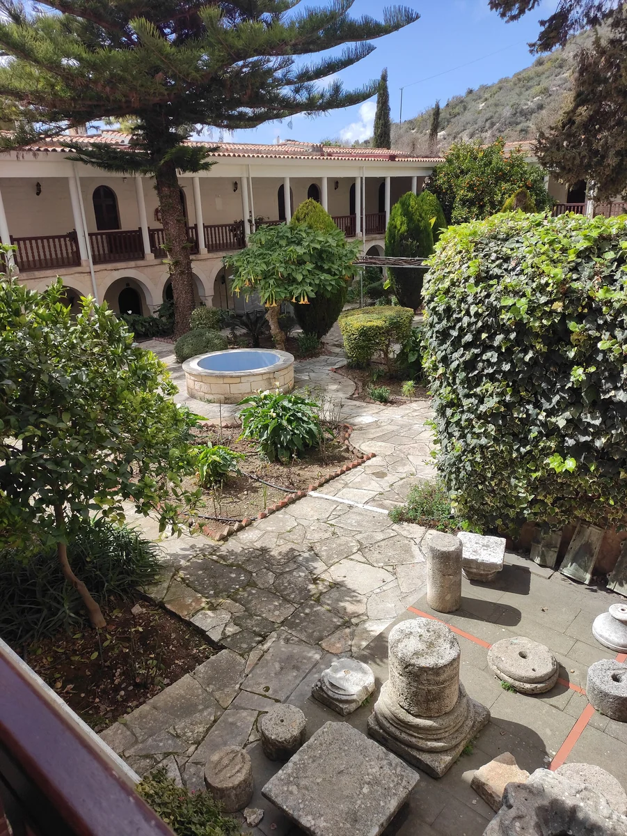 A garden courtyard with stone paths, architectural fragments and an arcaded building at Agios Neophytos Monastery in Tala, Cyprus; no cats are visible.